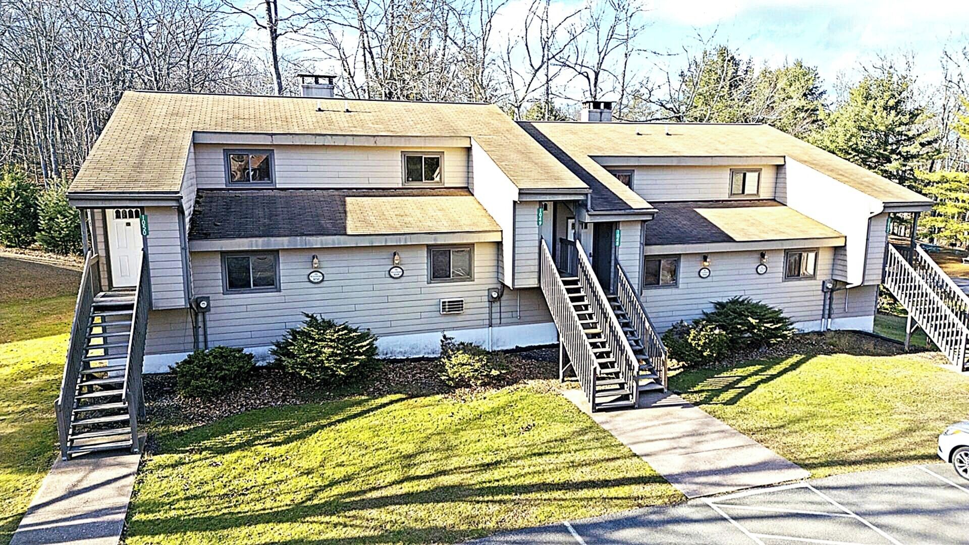 A two-story residential building with a central staircase, a small front porch, and a well-maintained lawn.