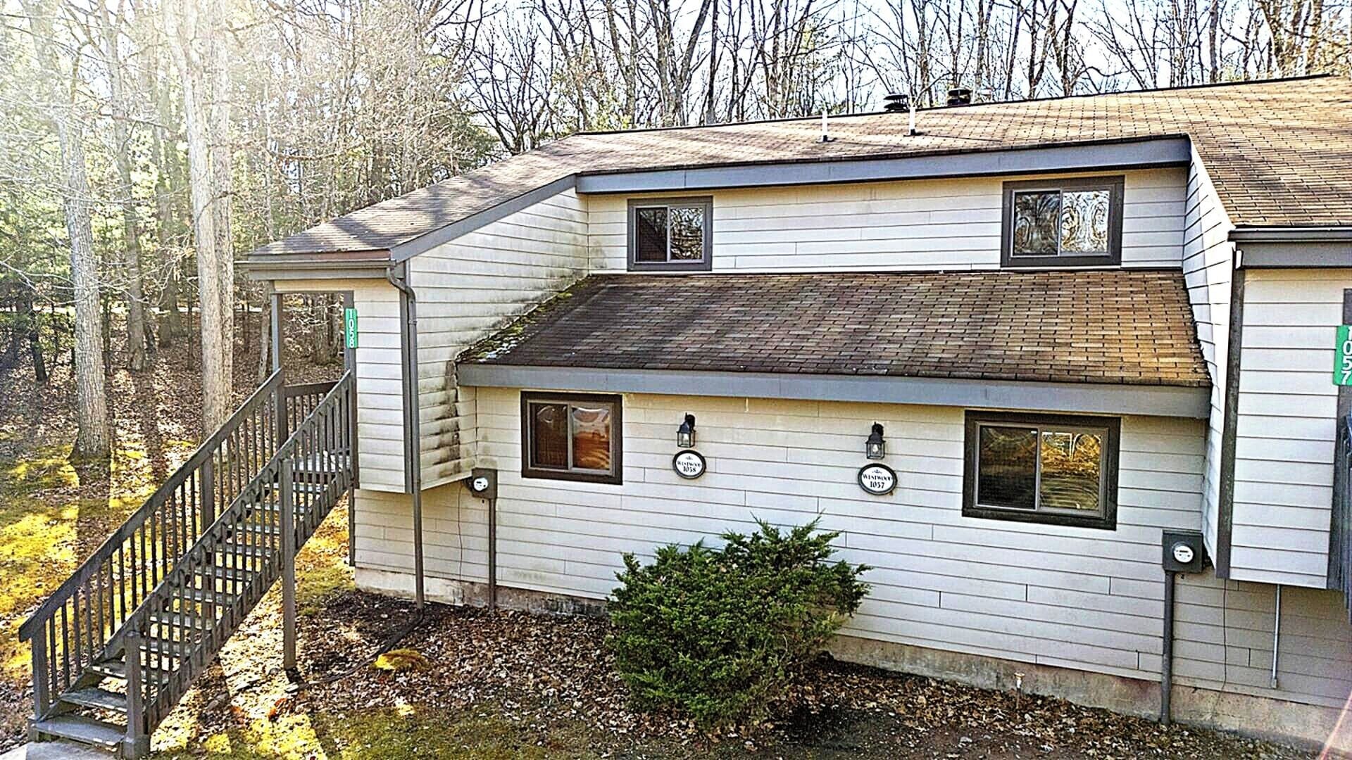 A two-story building with a staircase leading to the entrance, a small front porch, and a window with a sign.