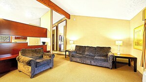 Ein Wohnzimmer mit einer Couch, einem Sessel, einem Holzschrank und einer Tür zu einem anderen Raum.