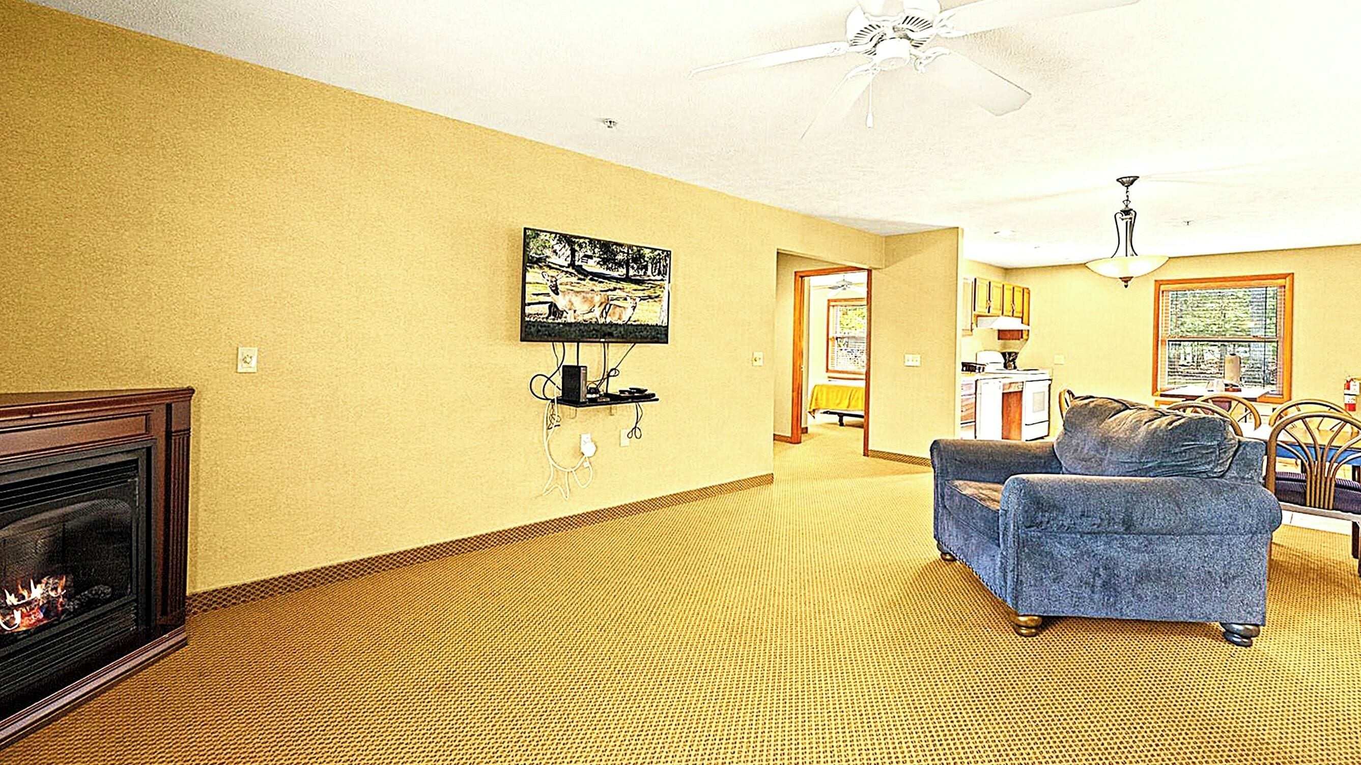 A living room with a fireplace, a television mounted on the wall, and a dining area with a table and chairs.