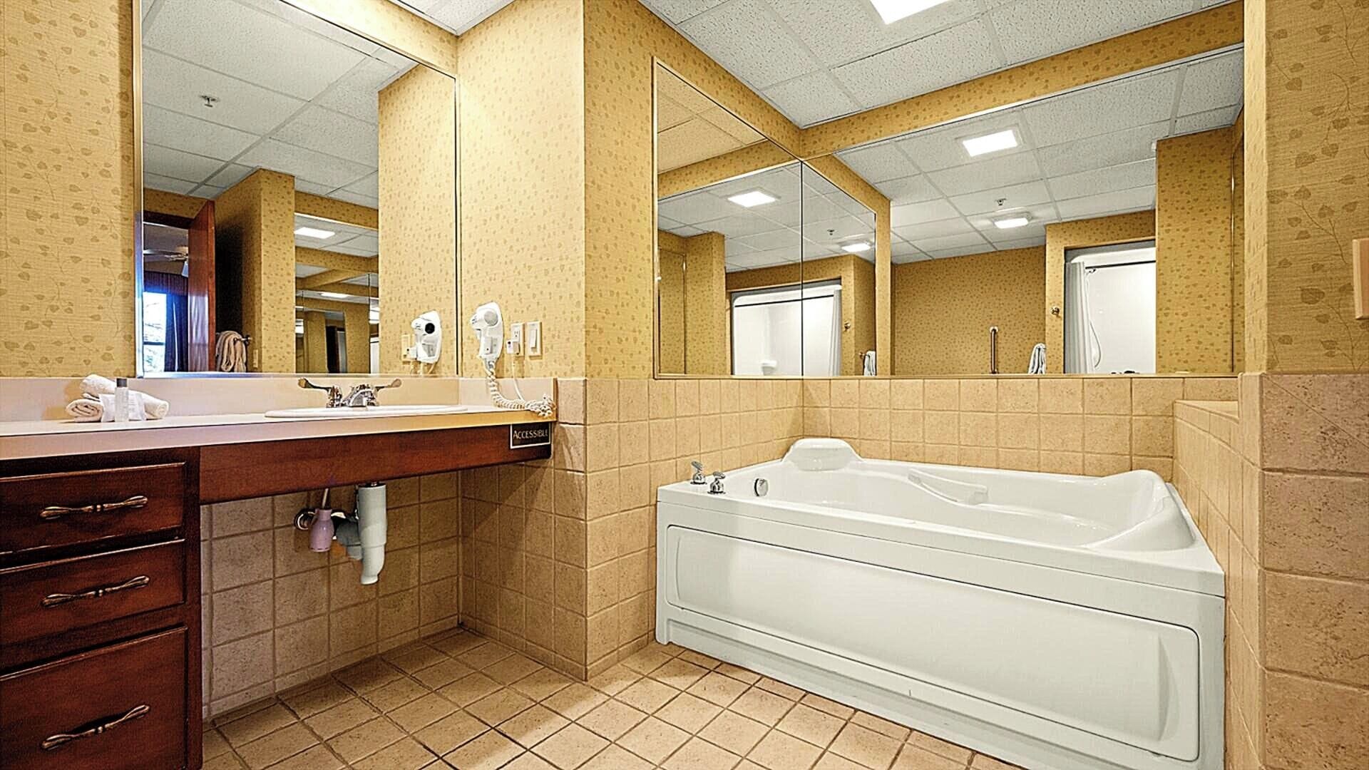 A bathroom with a large mirror, a sink, a vanity with drawers, a bathtub, and a towel rack.