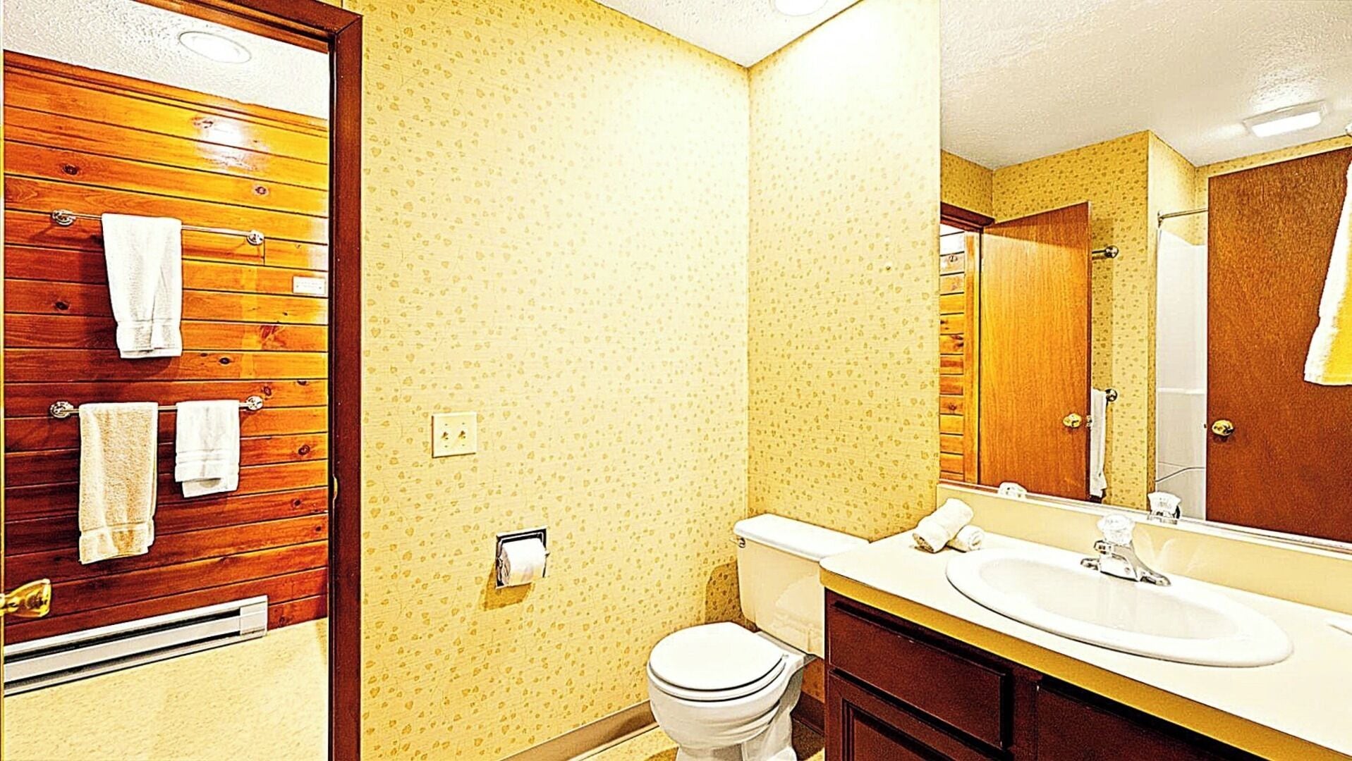 Une salle de bain avec des lambris en bois, des toilettes, un lavabo et un miroir.