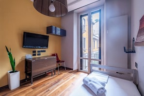 Ein modernes Schlafzimmer mit einem Holzkleiderschrank, einem Flachbildfernseher, einem Blumentopf, einem roten Sessel und einem großen Fenster mit Blick auf Gebäude.