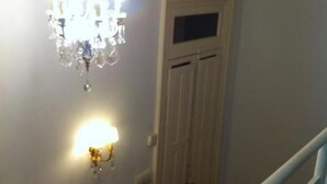 Un pasillo con candelabro y apliques en la pared, una puerta cerrada y una barandilla blanca.