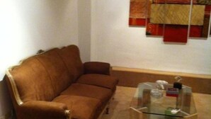 Un sofá marrón en una habitación con una mesa de centro de vidrio y un tapiz colgado en la pared.