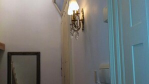 Un pasillo estrecho con un espejo a la izquierda, un aplique de pared y una puerta a la derecha.