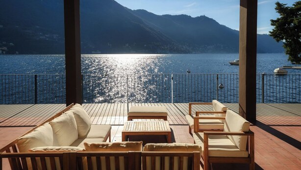 A covered outdoor seating area with wooden furniture and a view of a lake and mountains. - Villa Fisogni - App. 1 "Norma" (Moltrasio)