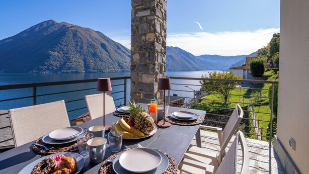 A table set for breakfast with a mountain view, a stone pillar, and a balcony railing. - Residence degli Oleandri - APP. A1 (Argegno)