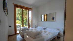 A bedroom with two beds, a large window, and a view of greenery outside. - Residence degli Oleandri - APP. A1 (Argegno)