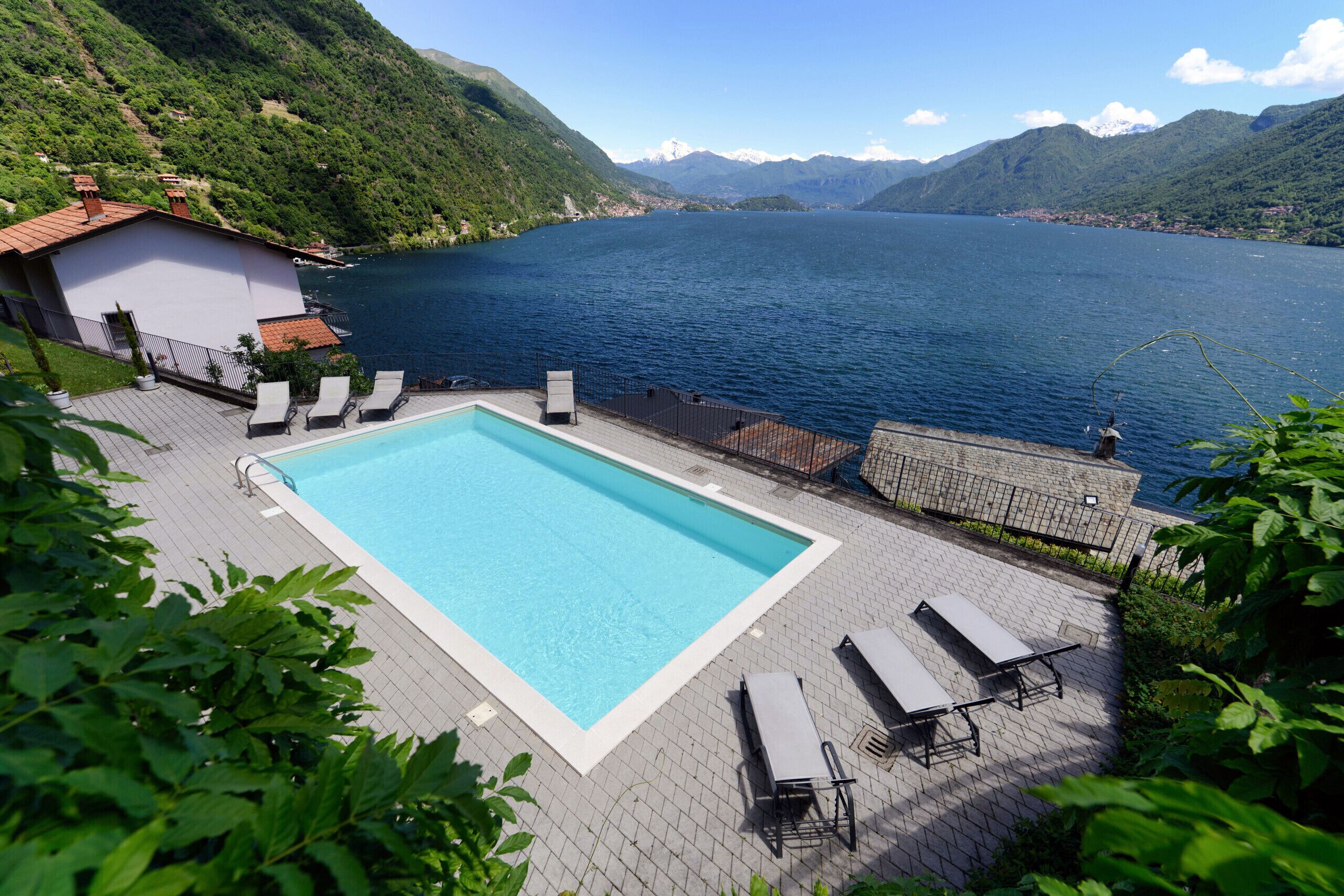 A swimming pool with lounge chairs, surrounded by a paved deck and a mountain backdrop.