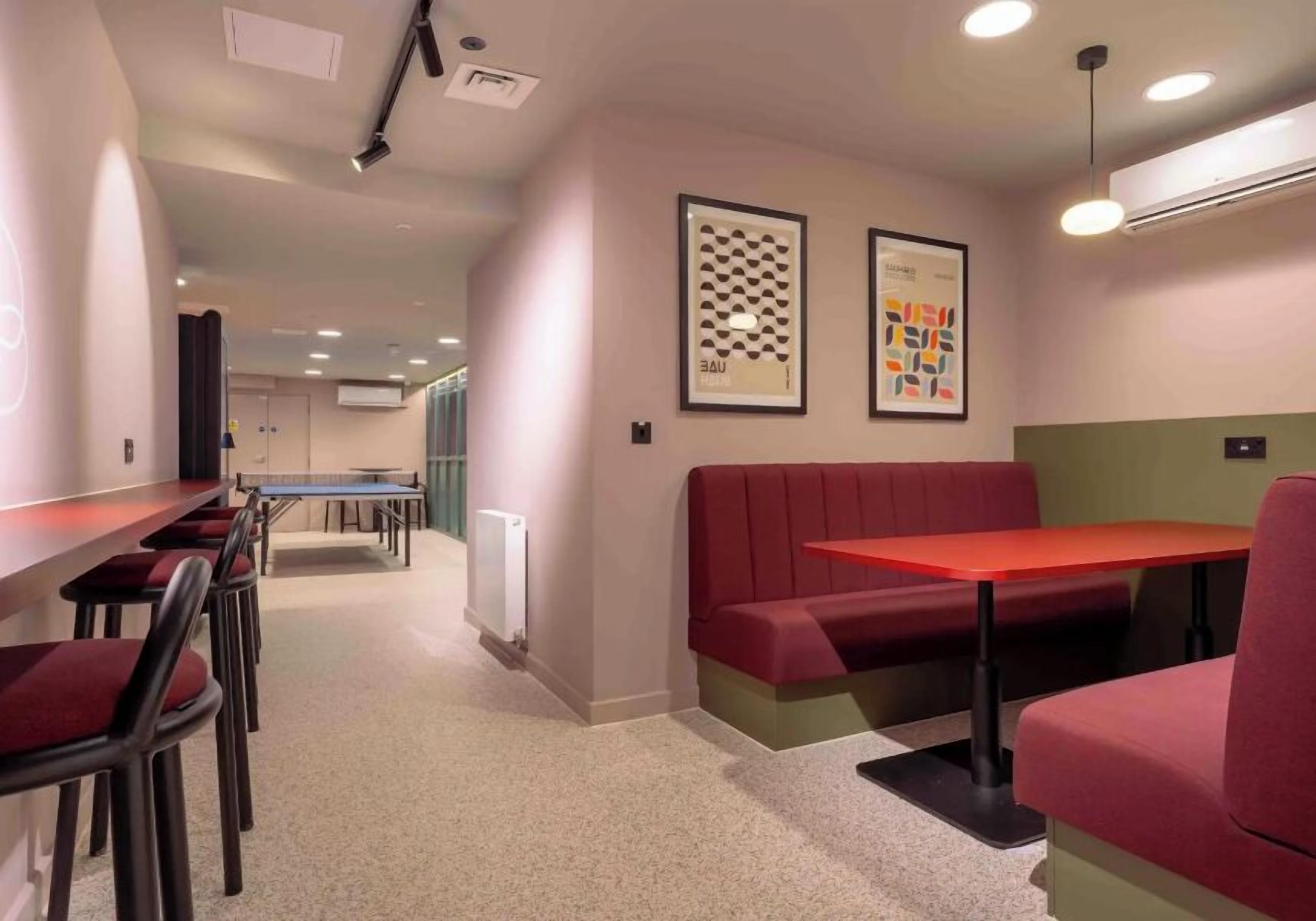 A modern lounge area with a pool table, red seating, and framed artwork on the walls.