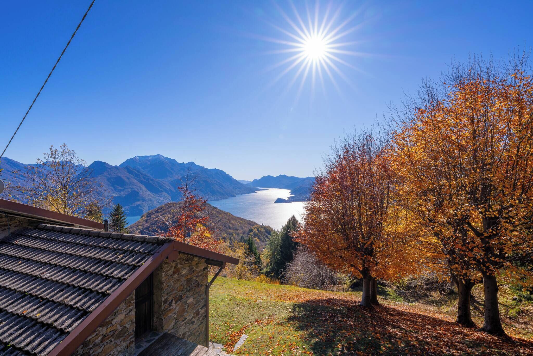 A mountain view with a lake, autumn trees, and a stone building with a tiled roof.