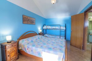 A bedroom with a bunk bed, a wooden nightstand with a lamp, and a painting on the wall.