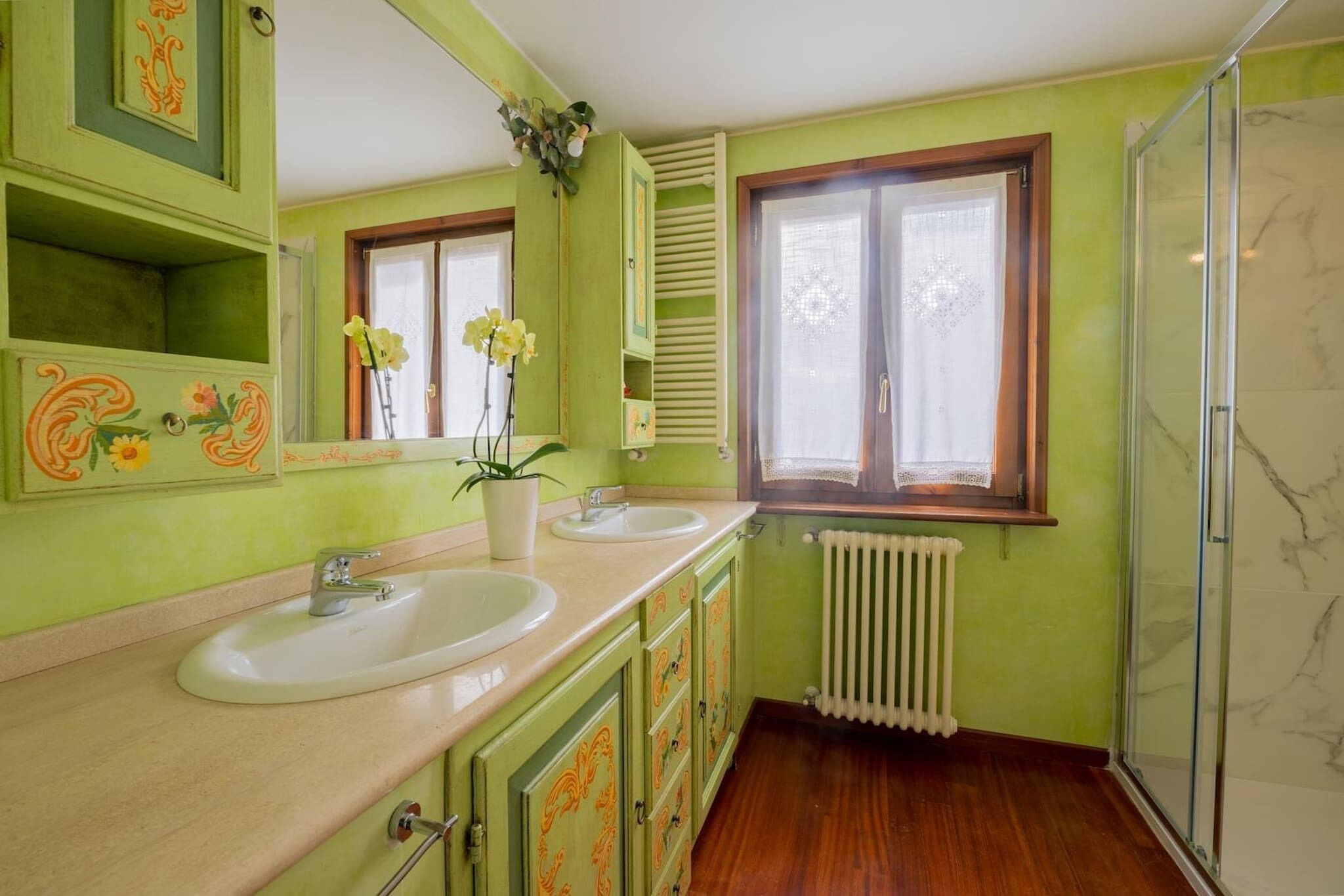A bathroom with two sinks, a mirror, a window with shutters, and a shower area.