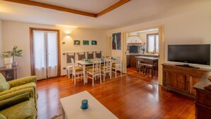 Zona d'estar àmplia amb taula de menjador, cadires, sofà, televisió i cuina al fons.