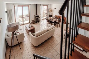 A spacious living room with a sofa, coffee table, and a dining table with chairs. There is a fireplace, a staircase, and a balcony with a view. - Apartment The View - Argegno (Argegno)