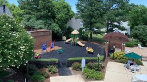 A playground with slides and a small playhouse, surrounded by trees and a patio area with outdoor seating. - 4th of July Week! - Williamsburg, ONLY => 26 Jun - 3 Jul 2027, Sleeps 12/4Br/4Ba (Williamsburg)