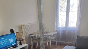 Ein Wohnzimmer mit einem Glastisch, einem grauen Sofa, einem weißen Esstisch mit Stühlen und einem Fernseher auf einem weißen Lowboard.