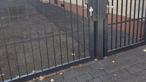 Ein durch einen Zaun gesicherter Bereich mit einem gepflasterten Weg und einem Gebäude mit Fenstern und einer Tür.