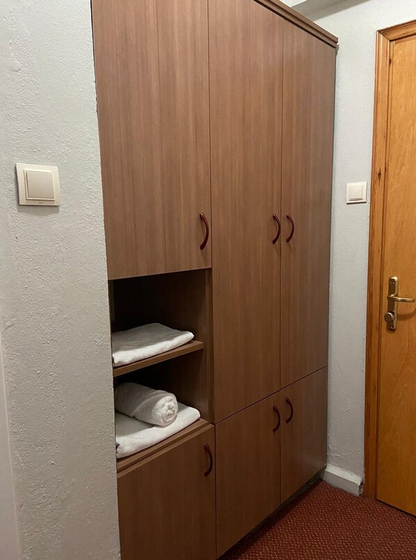 Une armoire en bois avec deux étagères et un placard inférieur, une porte dotée d’une poignée en laiton et un interrupteur sur le mur.
