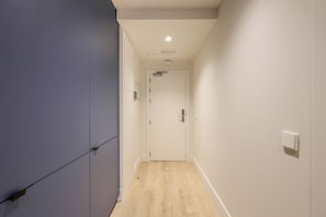 Un pasillo estrecho con suelo de madera, una puerta blanca al final y un interruptor de luz en la pared.