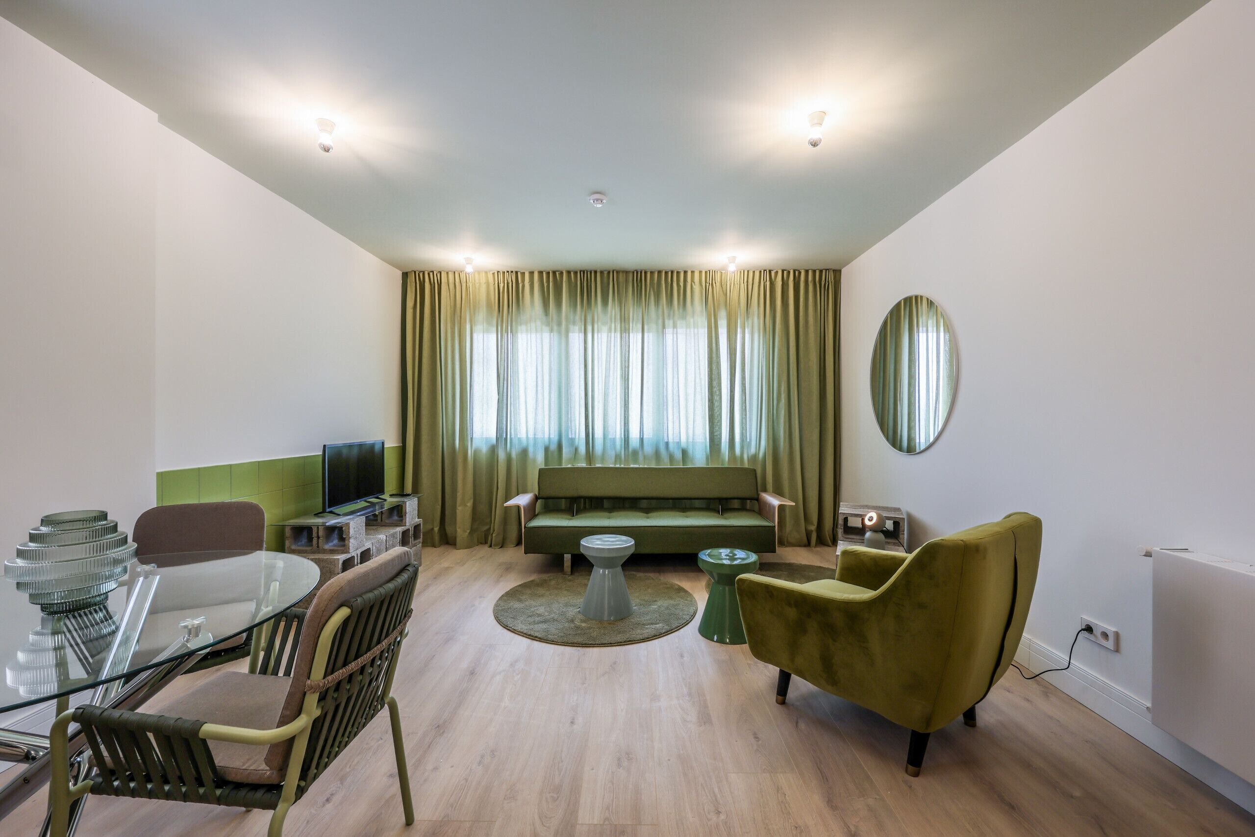 A modern living room with a glass dining table, a sofa, and a green armchair.