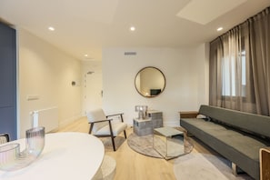 Una sala de estar moderna con un espejo redondo, un sofá gris, una mesa de comedor blanca y una mesa de centro gris.