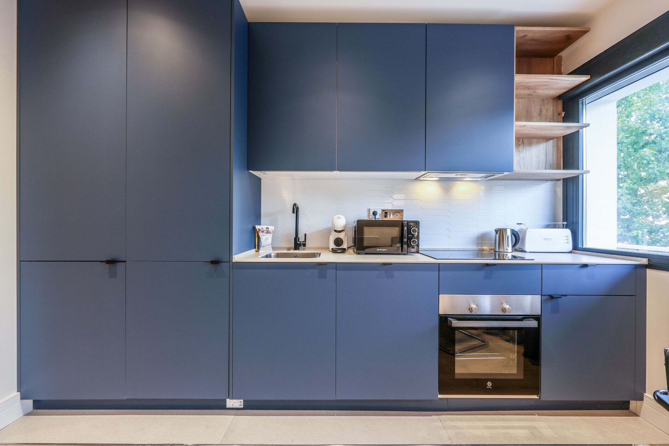 A modern kitchen with dark blue cabinets, a microwave, a toaster, and an oven.
