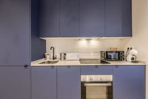 Una cocina compacta con armarios azul oscuro, una encimera blanca, horno empotrado, microondas, tostadora y hervidor.