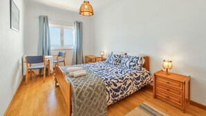A bedroom with a bed, bedside tables, a desk, chairs, and a window. - Holiday Home 'Ocean Villa Ericeira' with Sea View, Private Terrace and Wi-Fi (Ericeira)