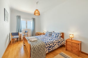 A bedroom with a bed, bedside tables, a desk, chairs, and a window. - Holiday Home 'Ocean Villa Ericeira' with Sea View, Private Terrace and Wi-Fi (Ericeira)