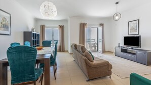 A modern living room with a dining area, a sofa, a TV, and a chandelier. - Holiday Home 'Ocean Villa Ericeira' with Sea View, Private Terrace and Wi-Fi (Ericeira)