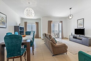 A modern living room with a dining area, a sofa, a TV, and a chandelier. - Holiday Home 'Ocean Villa Ericeira' with Sea View, Private Terrace and Wi-Fi (Ericeira)
