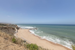 A coastal beach with a rocky cliff, a sandy shoreline, and a clear sky.