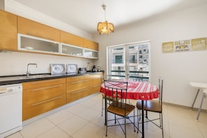 A kitchen with wooden cabinets, a white dishwasher, a red and white checkered table, and a window with a view of buildings.