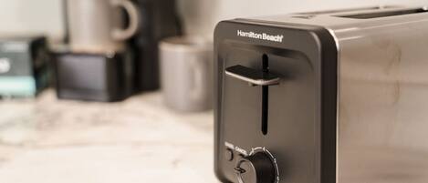 A Hamilton Beach toaster on a marble countertop with a coffee maker and mug in the background.