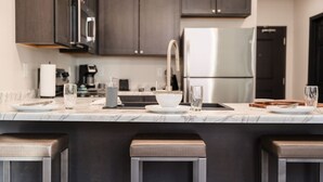 Une cuisine moderne avec des meubles de couleur sombre, un réfrigérateur en acier inoxydable et un plan de travail en marbre.