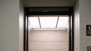 Un ascenseur avec une porte fermée, un panneau indiquant une sortie de secours en cas d’incendie et un sol antidérapant.