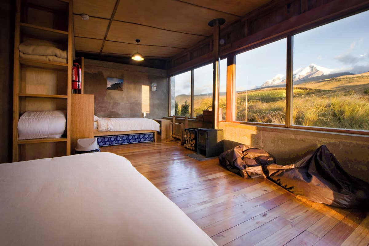 A bedroom with a bed, wooden shelves, a window with a mountain view, and a fire extinguisher.