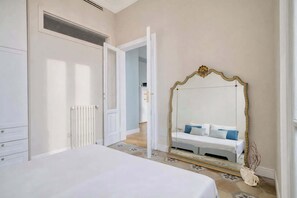 A bedroom with a large bed, a white dresser, a radiator, and a mirror with an ornate frame. - w*|  Bright 2BR Steps from Arco della Pace (Milano)