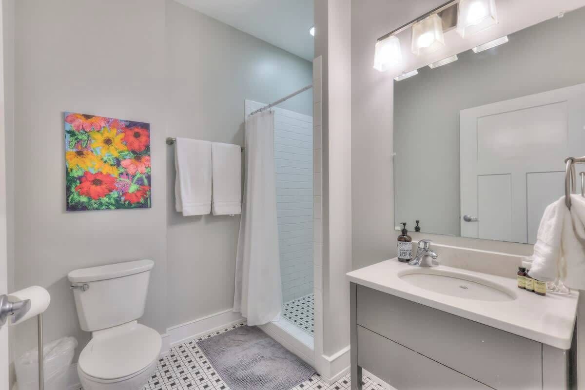 A bathroom with a toilet, shower, sink, and a mirror with lights.