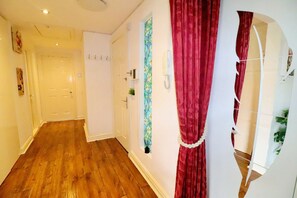 A hallway with wooden flooring, a white door, and a red curtain. - Luxurious 2BR Apartment| Free Parking | Lark Lane (Merseyside)