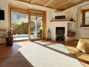 A spacious living room with a large sliding glass door leading to a snowy outdoor area, a fireplace, and a wooden ceiling. - Zur Schmiede - Alpchalet EG in Kaltenbrunn (Garmisch-Partenkirchen)