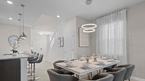 Een moderne keuken met een centraal eiland, een eetgedeelte met een witte tafel voor zes personen, en een trap naar een hoger niveau.
