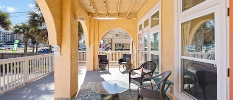 A covered outdoor seating area with tables and chairs, a patterned floor, and large windows.