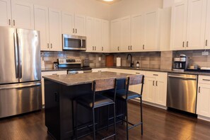 Una cocina moderna con electrodomésticos de acero inoxidable, una isla central con taburetes y un salpicadero de azulejos.