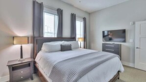 A bedroom with a large bed, two bedside tables with lamps, a flat-screen TV, and a door.
