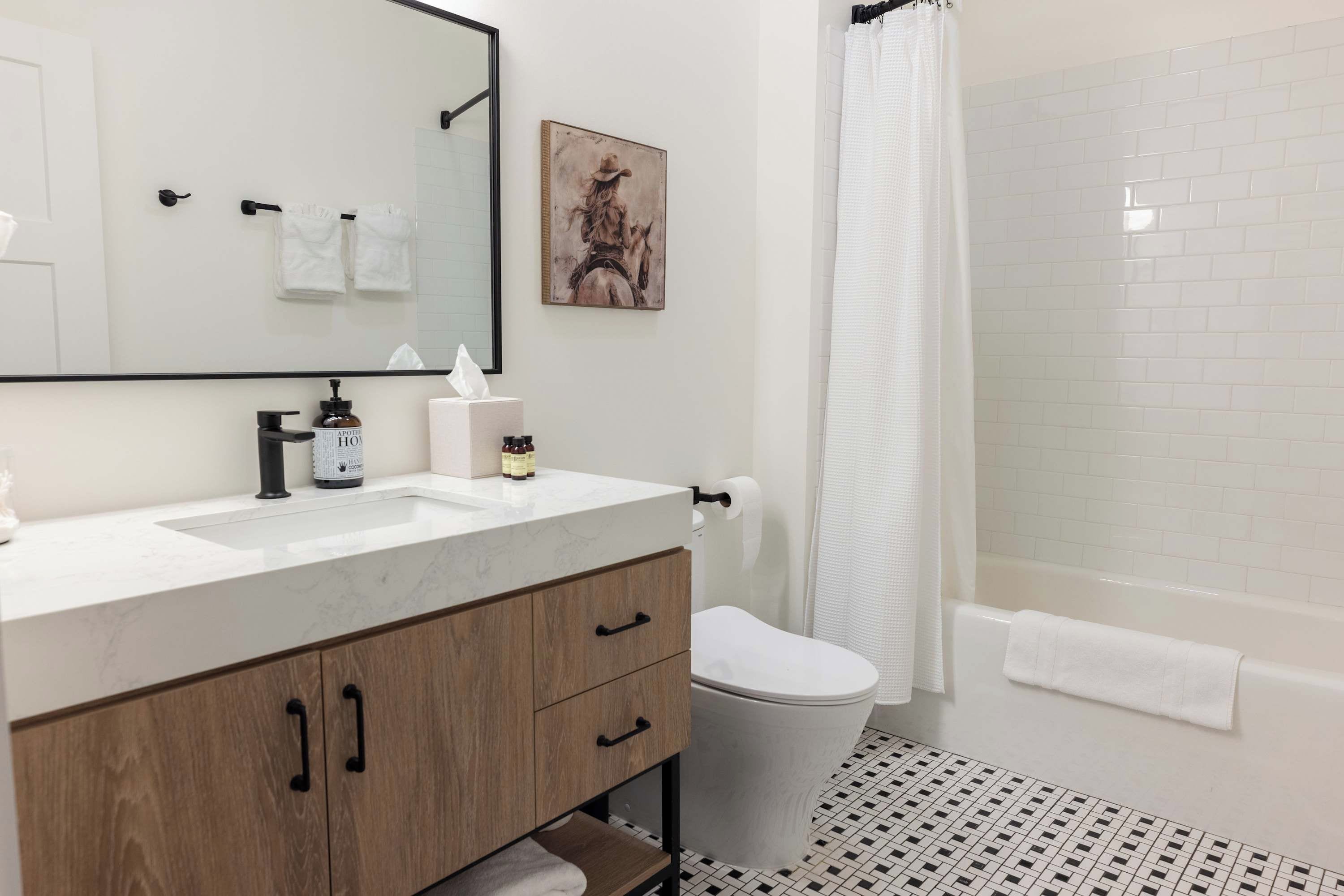 A bathroom with a white sink, wooden vanity, a toilet, and a shower area.