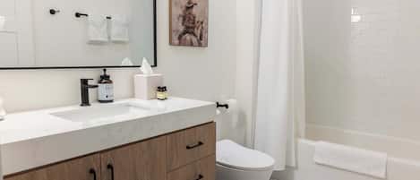 A bathroom with a white sink, wooden vanity, a toilet, and a shower area.