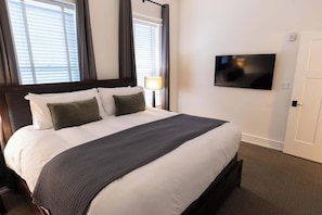 Una habitación de hotel con una cama grande, un televisor de pantalla plana en la pared y una ventana con persianas.